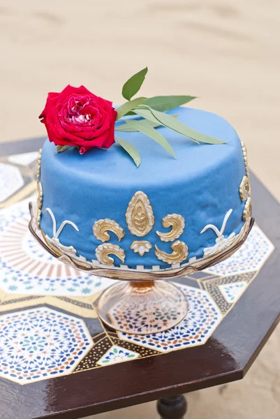 Blue wedding cake on a table and red roses on top in the desert landscape