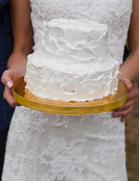 White wedding cake in hands of the bride