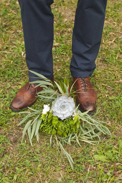 Young fashion man\'s legs in blue jeans and brown boots on grass with brides bouquet