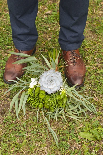 Young fashion man\'s legs in blue jeans and brown boots on grass with brides bouquet