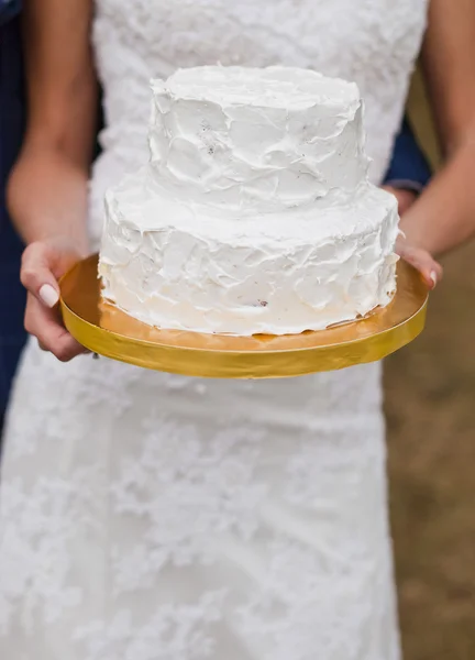 White wedding cake in hands of the bride