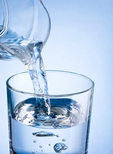 Close-up pouring water from a jug into glass on a blue backgroun