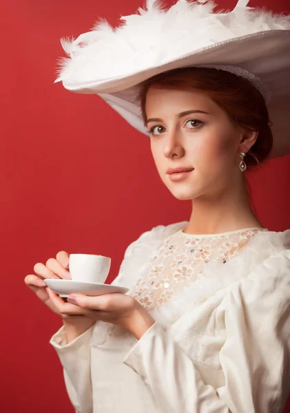 Portrait of redhead edwardian women with cup on red background.