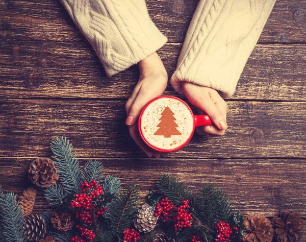 Female holding cup of coffee with cream christmas tree on a tabl