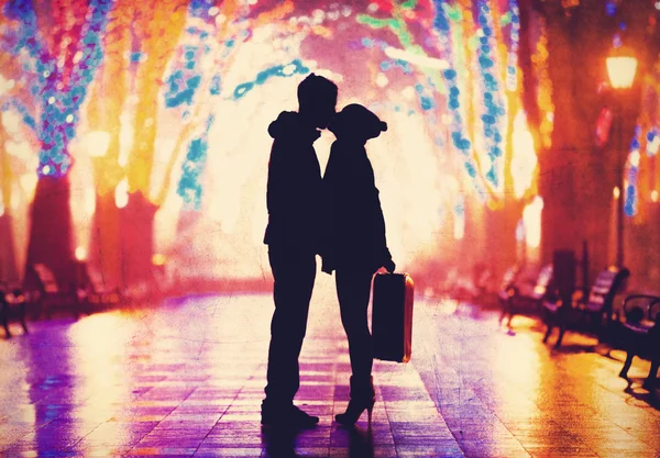 Couple with suitcase kissing at night alley.