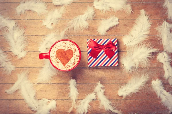 Coffee and feathers with gift on wooden background.