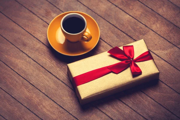 Cup of coffee and gift box on a wooden table.