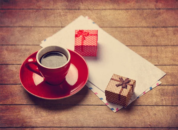 Cup of coffee and gift box with envelopes on a wooden table.