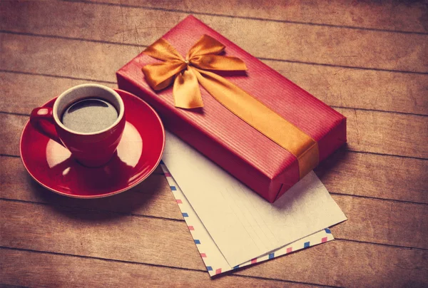 Cup of coffee and gift box with envelopes on a wooden table.
