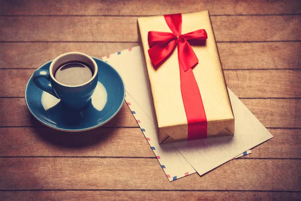 Cup of coffee and gift box with envelopes on a wooden table.