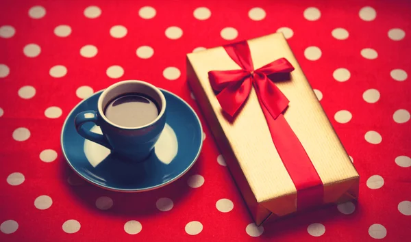 Cup of coffee and gift box on a polka dot background.