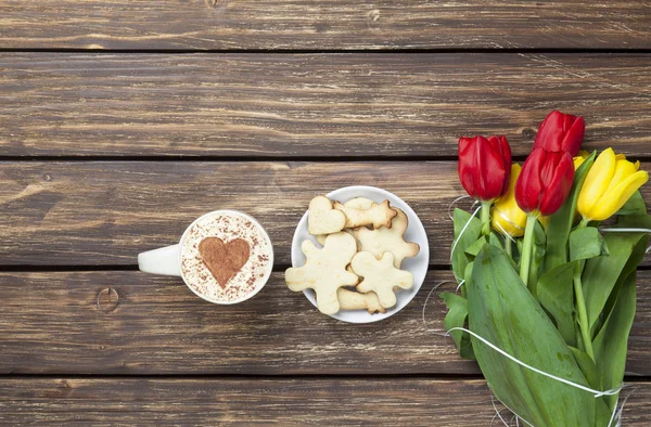 Cup of cappuccino with heart shape and bouquet of tulips with co