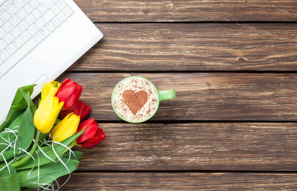 Cup of cappuccino with heart shape and computer