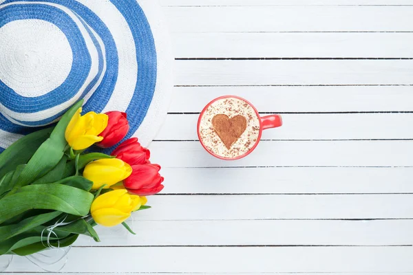 Cup of cappuccino with heart shape and bouquet of tulips