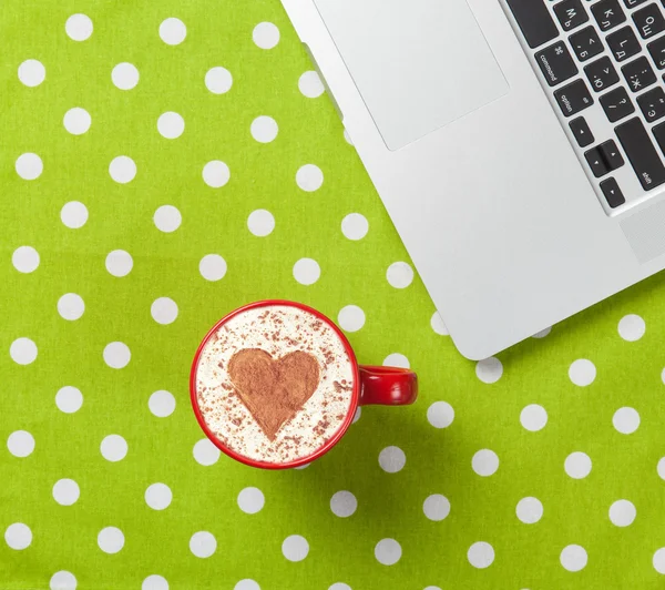 Cup of cappuccino with heart shape and laptop