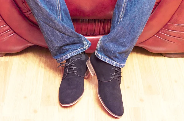 A man in jeans and shoes on a leather sofa