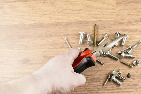 Pliers in hand on a background of various bolts