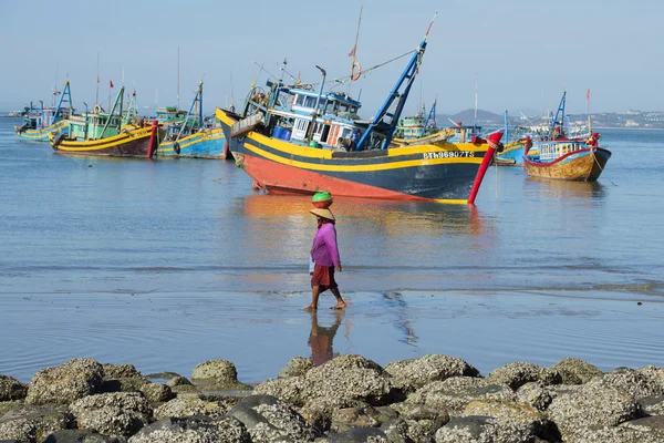 Vietnamese woman walking on the coastal strip on the background of fishing boats. The fishing harbour of Mui Ne, Vietnam
