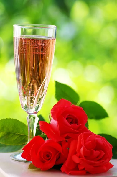 Rose wine in glass and roses on green background