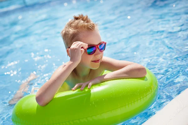 Little boy swimming in the pool with big bright green rubber ring, having fun in aquapark.