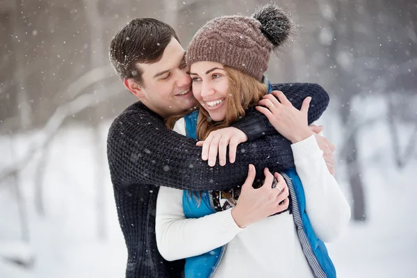 Young couple in love walking in winter park. It\'s snowing, winter. Young man embraces the girl. She laughs.