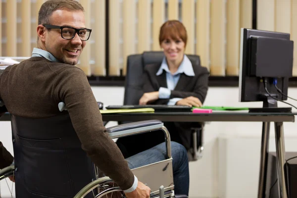 Smiling man on wheelchair looking towards the camera while femal