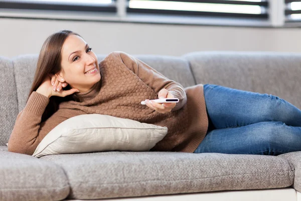 Smiling woman lying on the sofa while looking tv