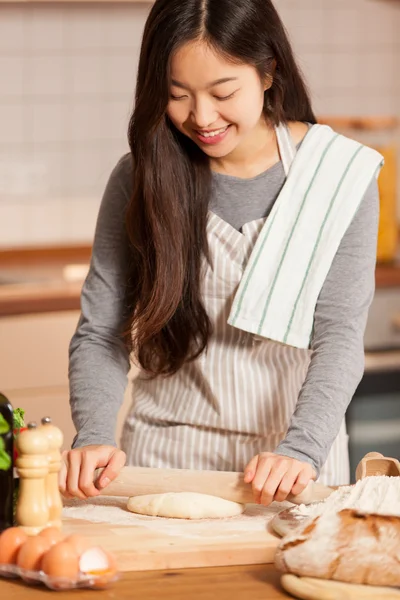 Asian young woman is baking bread in her home kitchen
