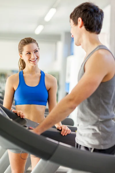 Female fitness instructor smiling towards young man on a treadmi