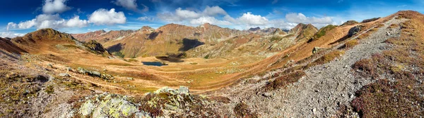 The picturesque top view on the valley between the mountains, hills, mountain slopes with dry yellow grass on a background of blue sky with clouds in the autumn