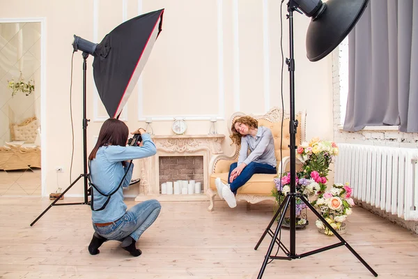 Woman photographer in a studio making portrait photo shoot session for young woman. Softbox flash and other impulse light equipment in the interior of photographic studio