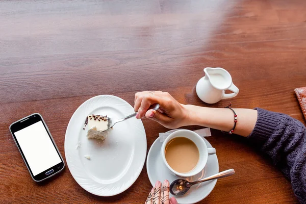 Smart phone, espresso, cake and female hand composition on table