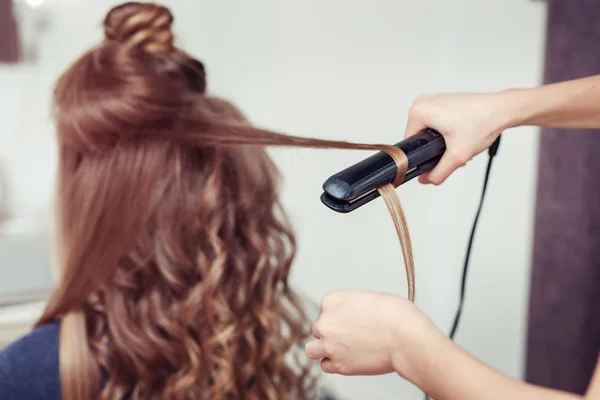 Closeup of hairdresser doing hairstyle with hair iron