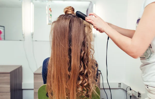 Hairdresser making hairdo for girl with curly golden hair with c