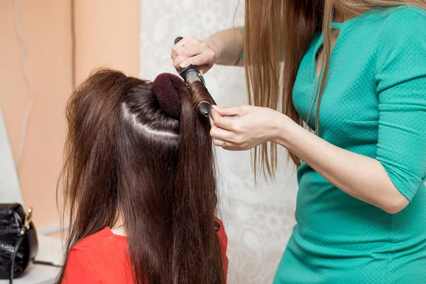 Stylist in barber salon using curling iron for brunette hair cur