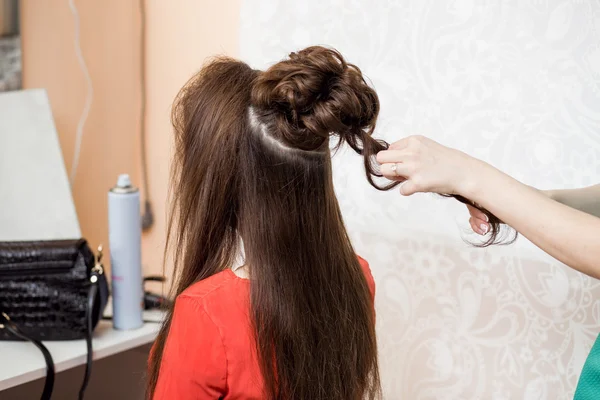 Hairdresser make evening hairstyle on brown hair in beauty salon