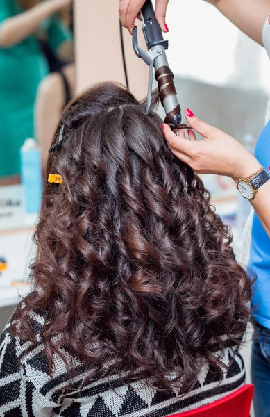 Stylist using curling iron for hair curls, close-up, shot in bar