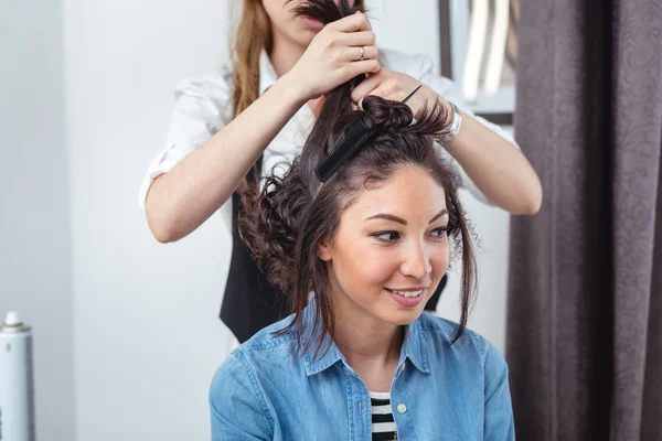 Hair stylist making ringlets to a happy brunette woman. Hairdres