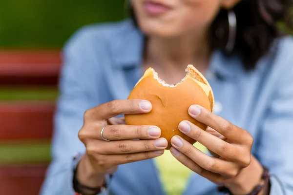 Young woman outdoors eating a fast food hamburger. Focus on the