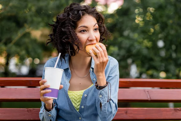 Young woman enjoying a fast food chicken burger and soda water o