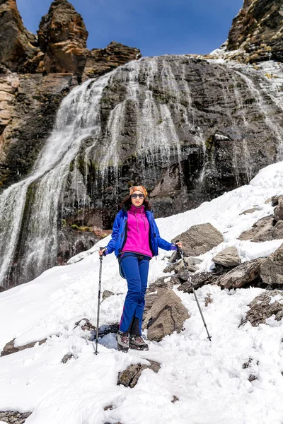 Girl hiker enjoying mountain waterfall with snow at early spring
