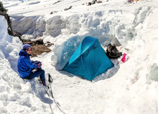 Woman climber sitting in the camp near the tent. The camp is protected from the wind by a wall of snow