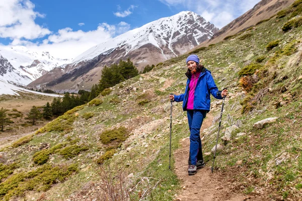 Woman hiker trekking in Caucasus mountain trail, walking with trekking poles