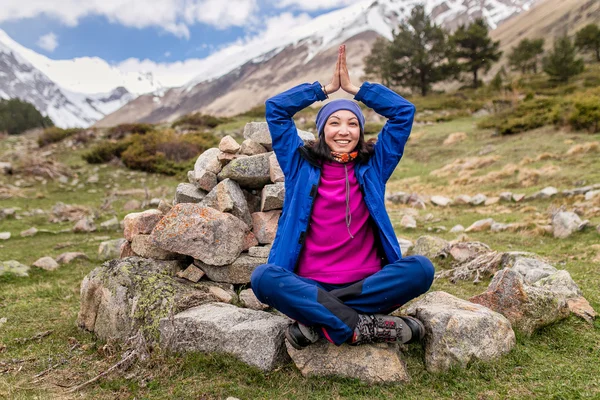 Young woman sitting in yoga pose in mountains between spiral of stones