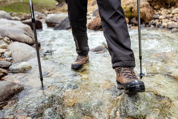 Man in trekking boots hiking outdoor and wading river or creek eith stones on background. Lifestyle, Travel or survival concept top view
