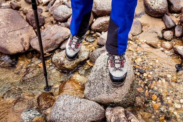 Waterproof trekking boots wade a rocky mountain stream. The concept of high quality hiking equipment