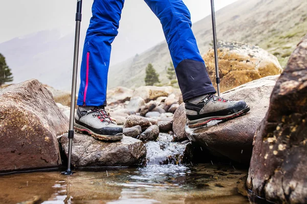 Waterproof trekking boots wade a rocky mountain stream. The concept of high quality hiking equipment