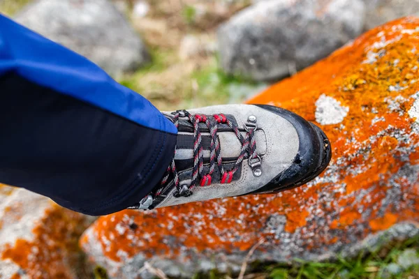 Trekking and hiking boots walking on the orange lichen covered stones. Concept of quality hiking shoes