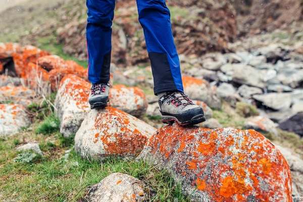 Trekking and hiking boots walking on the orange lichen covered stones. Concept of quality hiking shoes