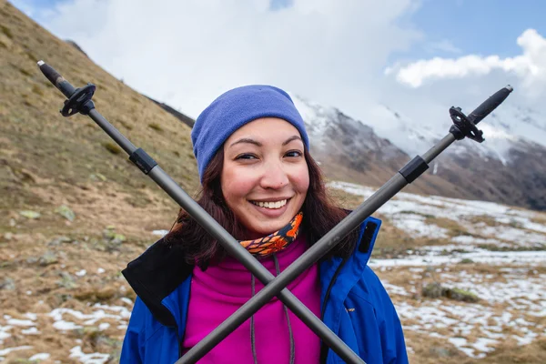 A happy young woman while hiking in the high mountains raised up her trekking poles